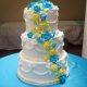 Tasty Pastry Custom Cakes: Three-tiered cake with white icing & cascading blue/yellow icing flowers