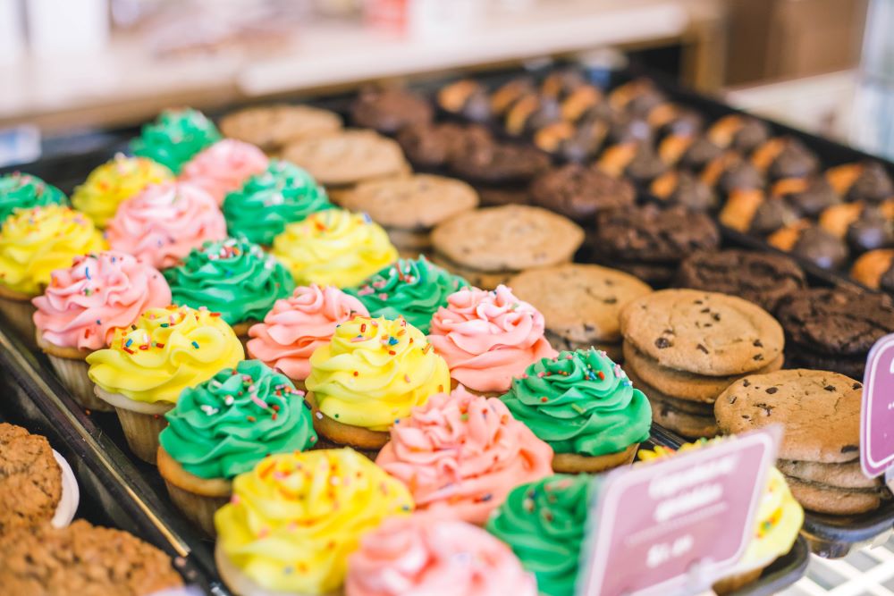 Tasty Pastry Display showing assortment of baked goods including: cupcakes with green, yellow or pink icing & sprinkles and cookies (chocolate chip, chocolate, oatmeal raisin)