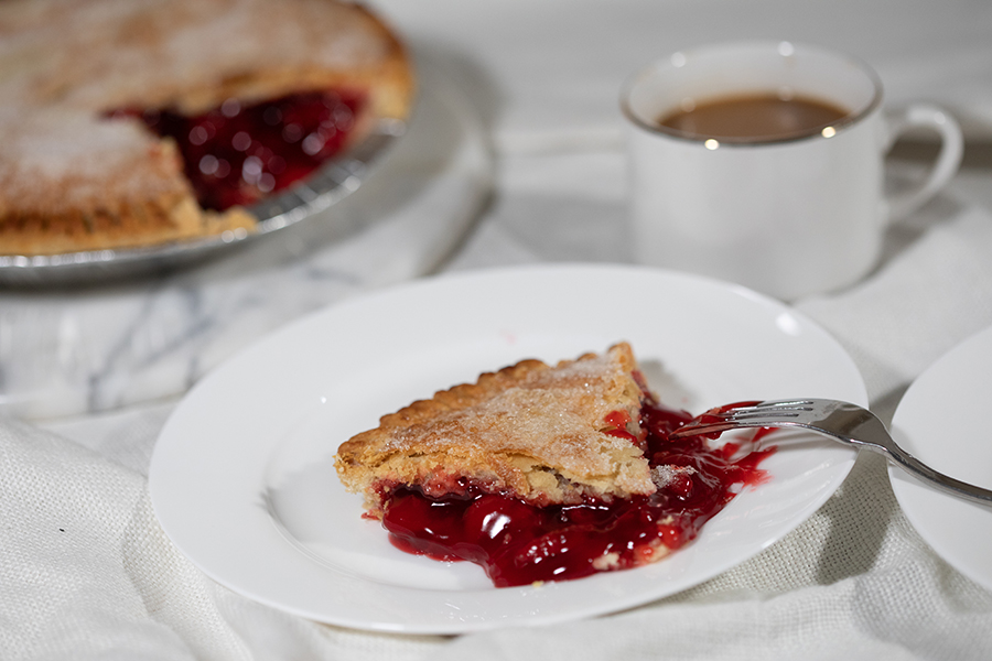 Tasty Pastry Pies: A slice of cherry pie on a white plate with a fork; a cup of coffee and the remaining pie in the background