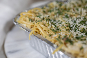 Casserole with Spaghetti noodles topped with herbs and grated cheese in a casserole carryout dish